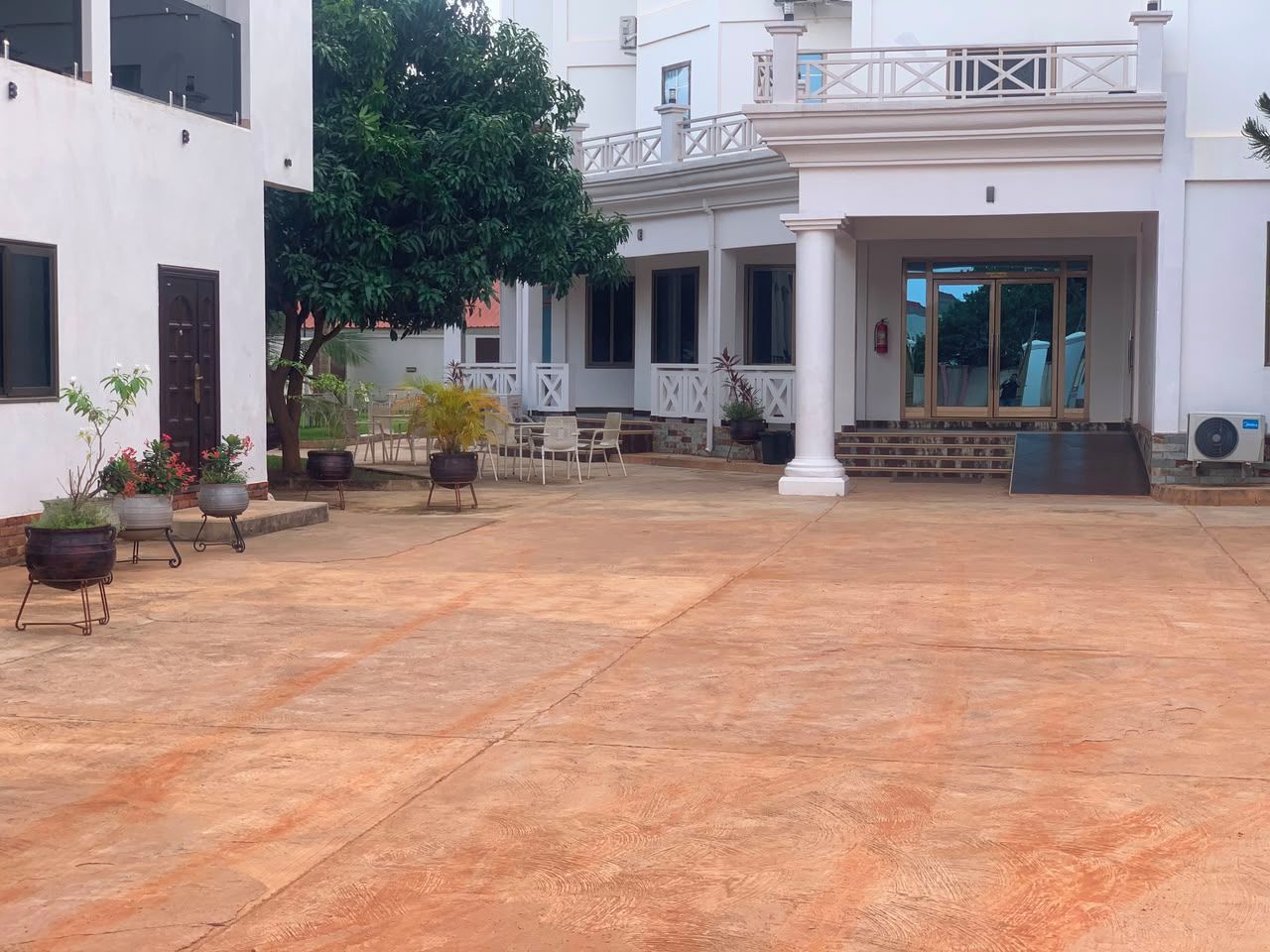 Un patio con un edificio blanco, plantas en macetas y una zona de estar cubierta.