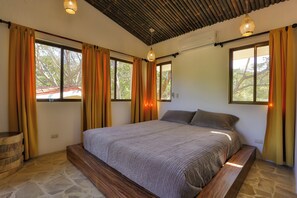 A bedroom with a large bed, wooden headboard, stone flooring, and multiple windows with curtains. - Casa Colibri Vista Ocotal 12 - 4BR condo & pool/ walking distance to Playa Ocotal (Playa Ocotal)
