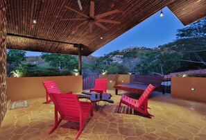 An outdoor patio with a wooden ceiling, red chairs, a table, and a view of a hillside with buildings. - Casa Colibri Vista Ocotal 12 - 4BR condo & pool/ walking distance to Playa Ocotal (Playa Ocotal)