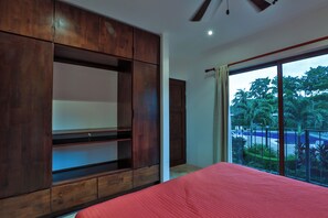 A bedroom with a large bed, wooden wardrobe, and a sliding glass door leading to a balcony with a view of greenery and a pool. - Casa Colibri Vista Ocotal 12 - 4BR condo & pool/ walking distance to Playa Ocotal (Playa Ocotal)