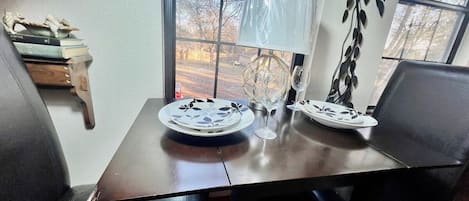 A dining table with plates and a wine glass, a window with a view of trees, and a wall-mounted decoration.
