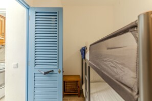 A bedroom with a bunk bed, a wooden bench, a door with horizontal slats, and a small table. - #424 Sea View | 3BR & Balcony | Olhos de Água (Albufeira)
