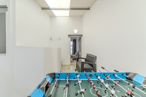 Una habitación con mesa de fútbol, una silla y una puerta que da a otra habitación.