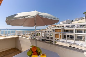 A balcony with a table, fruit, and drinks, overlooking a beach and buildings. - #424 Sea View | 3BR & Balcony | Olhos de Água (Albufeira)