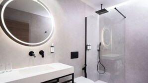 A modern bathroom with a round mirror, a white sink, a toilet, and a glass-enclosed shower. - Alora Hotel Madrid Alcorcón (Alcorcón)