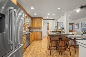 A modern kitchen with wooden cabinets, a stainless steel refrigerator, and a central island with bar stools. - Abode on Norfolk, Old Town PC home, hot tub, walk to Town Lift (Park City)