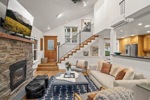 A spacious living area with a fireplace, a staircase leading to a second floor, and a kitchen with wooden cabinets. - Abode on Norfolk, Old Town PC home, hot tub, walk to Town Lift (Park City)