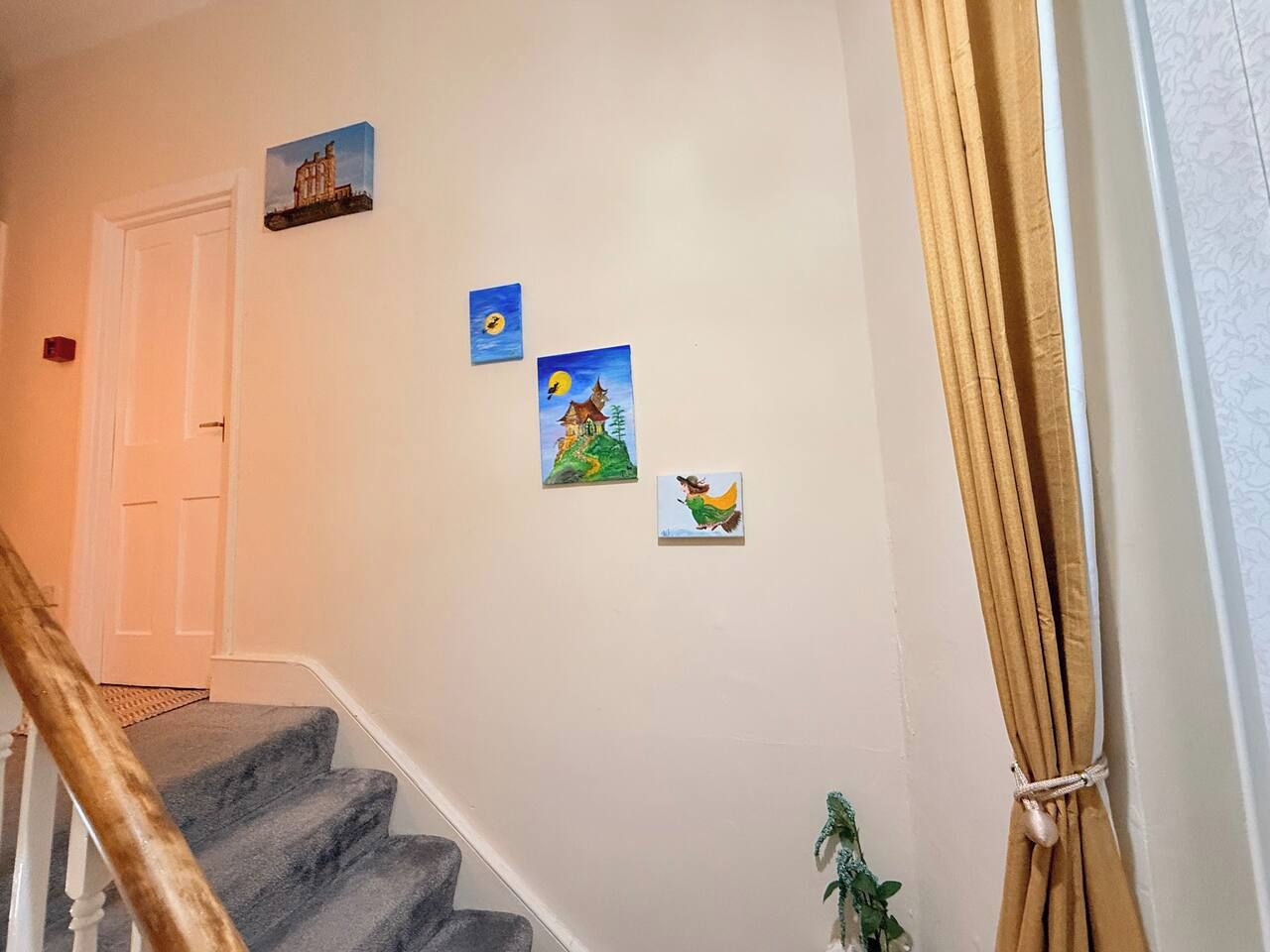 A staircase with a handrail, a door at the top, and three small paintings on the wall.