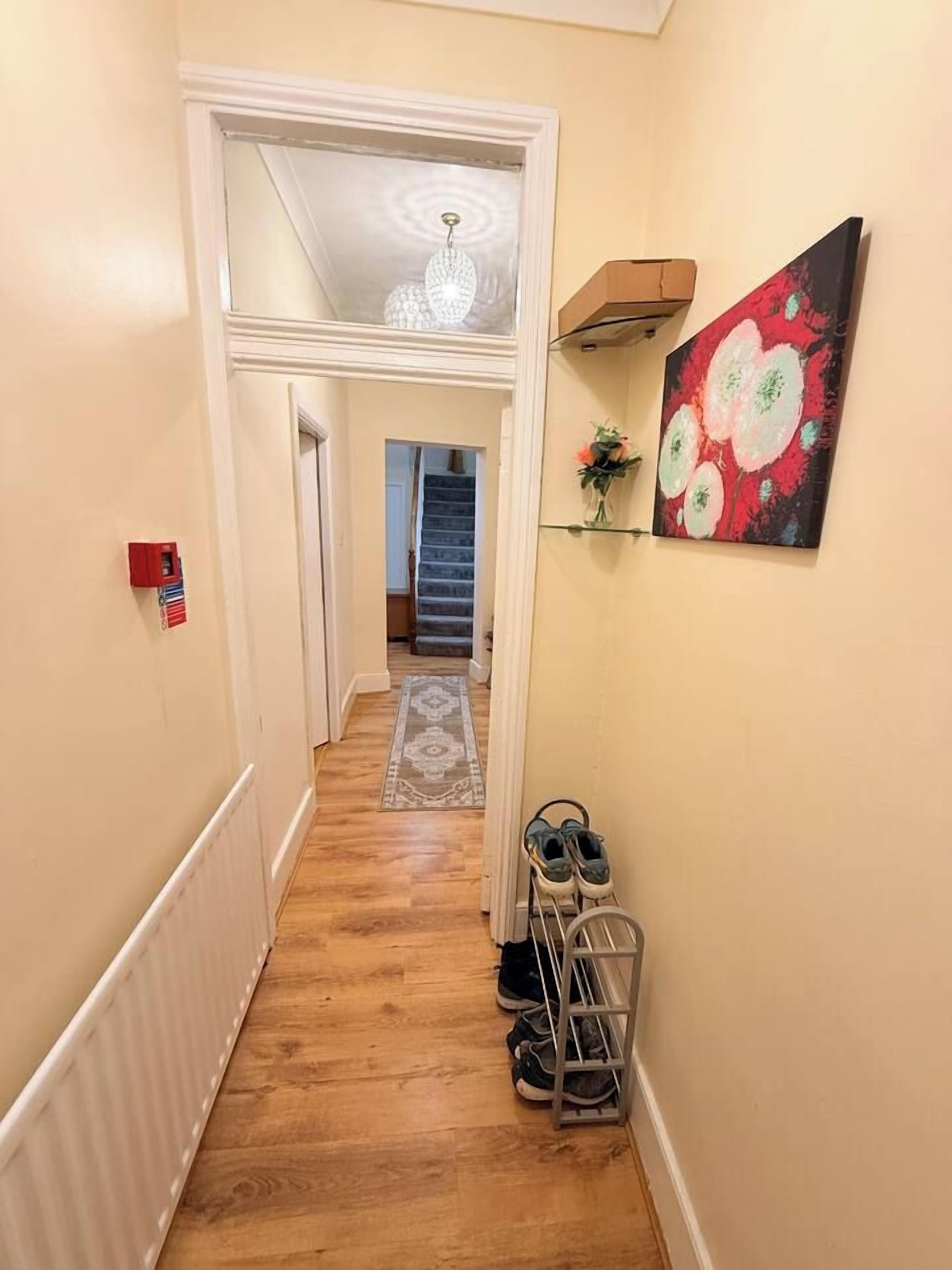 Un couloir avec un plancher en bois, un radiateur, un porte-chaussures et un tableau accroché au mur.