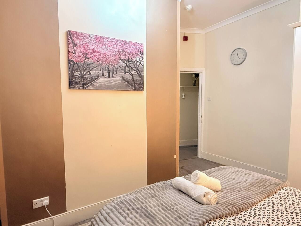 Un dormitorio con una cama, un cuadro en la pared, un reloj y una puerta que da a otra habitación.