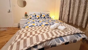Ein Schlafzimmer mit Bett, Nachttisch, Lampe und Vorhängen.