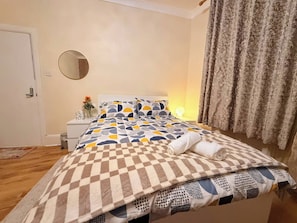 A bedroom with a bed, bedside table, lamp, and curtains. - Spacious 4BR House | 5 Mins to city | Sleeps 9 (Tyne and Wear)