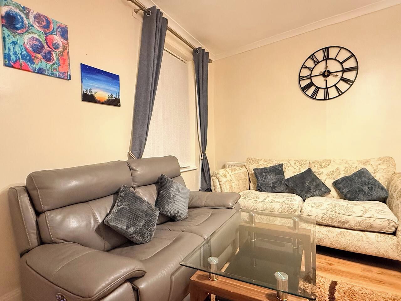 Un salon avec un canapé en cuir, une table basse en verre, un canapé à motifs et une horloge murale.