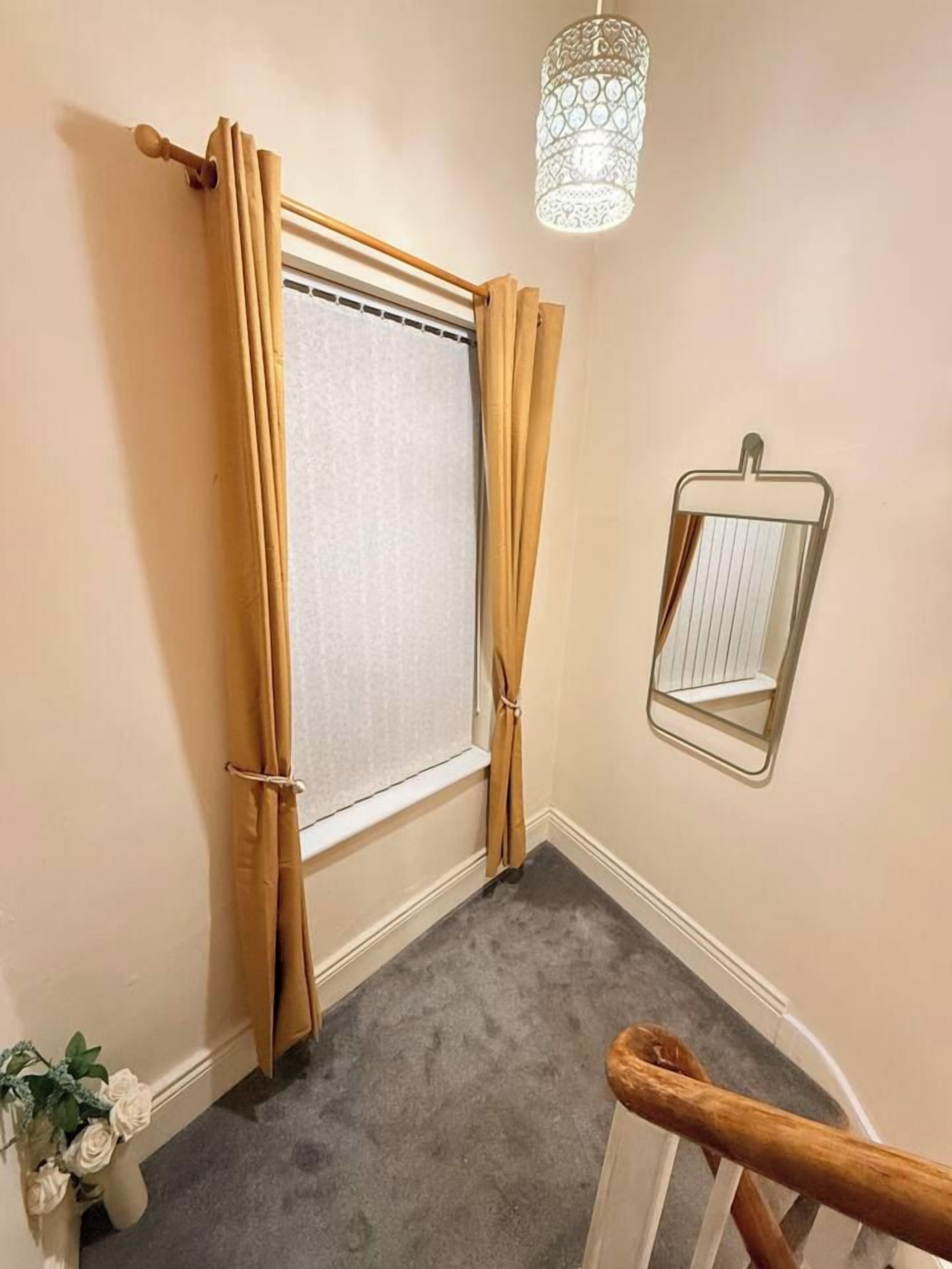 Une pièce avec une fenêtre, un miroir, un luminaire et un sol recouvert d’une moquette.