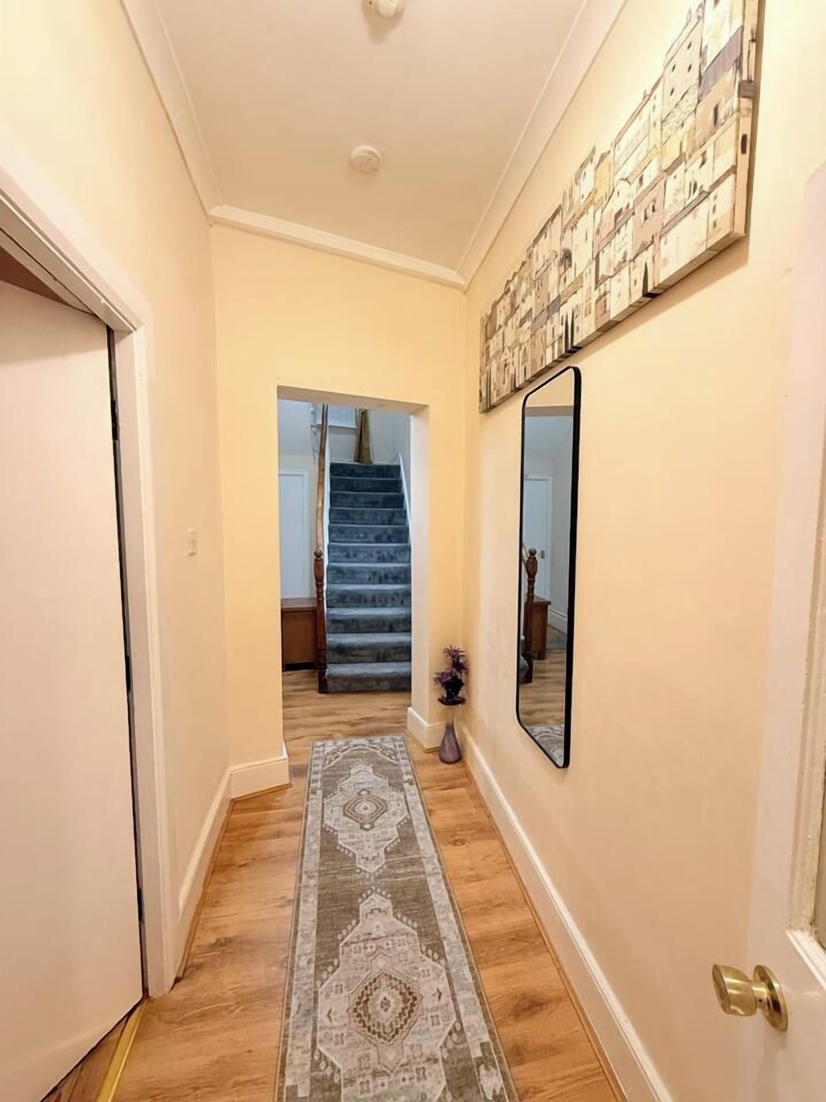 Ein Flur mit Holzboden, einem gemusterten Teppich, einer Treppe und einem an der Wand befestigten Spiegel.