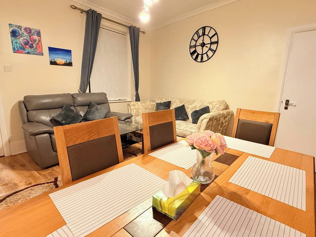Un coin repas avec une table en bois, des chaises, un vase de fleurs et un jeu de fléchettes accroché au mur.
