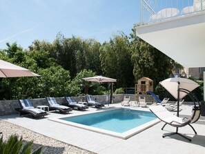 Ein Pool mit Liegestühlen und Sonnenschirmen, umgeben von viel Grün.