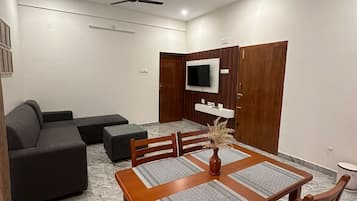 A modern living room with a dining area, a sofa set, a TV mounted on the wall, and ceiling fans.