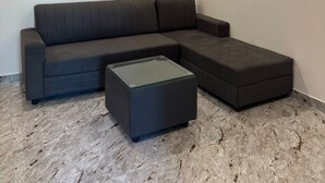 A modern living room with a sectional sofa, a glass coffee table, and a ceiling fan. - MV Home Stay (Thirumangalam)