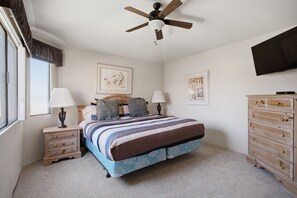Quarto com cama, mesas de cabeceira, cômoda, ventilador de teto e obras de arte nas paredes.