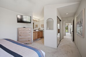 Une chambre à coucher comprenant un lit, une commode, un téléviseur et une salle de bain avec un lavabo et un miroir.