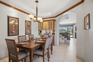 A dining area with a wooden table and chairs, framed artwork on the walls, and a view of a balcony with a railing. - Palm Valley Oasis with Golf Course & Lake Views (Palm Desert)