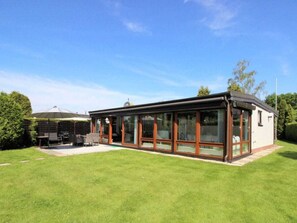 A modern house with a glass conservatory, a patio, and a well-maintained lawn. - Holiday Home With 4 Bedrooms (Scharbeutz)
