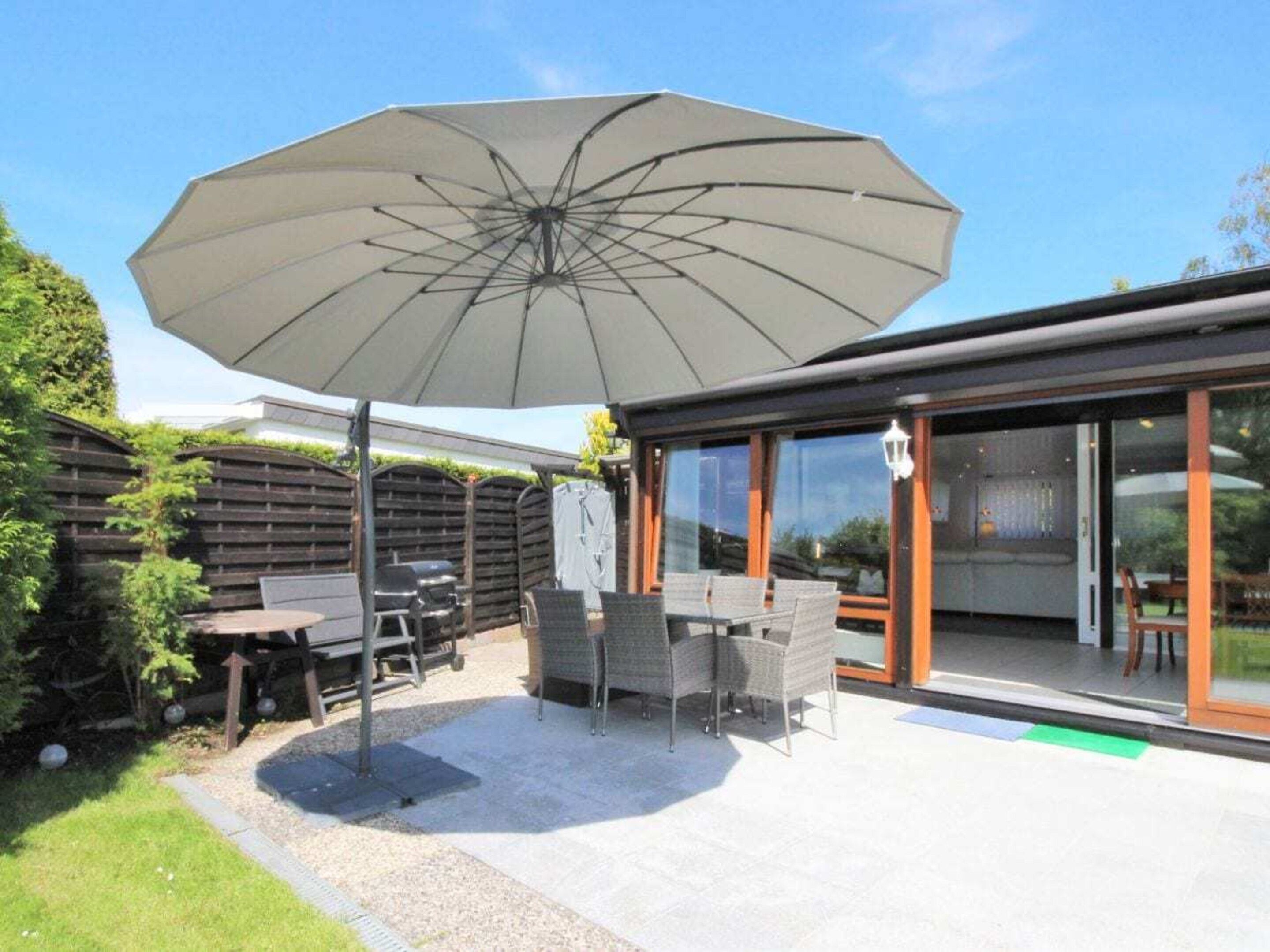 An outdoor patio with a table and chairs, a large umbrella, and a glass-enclosed area.
