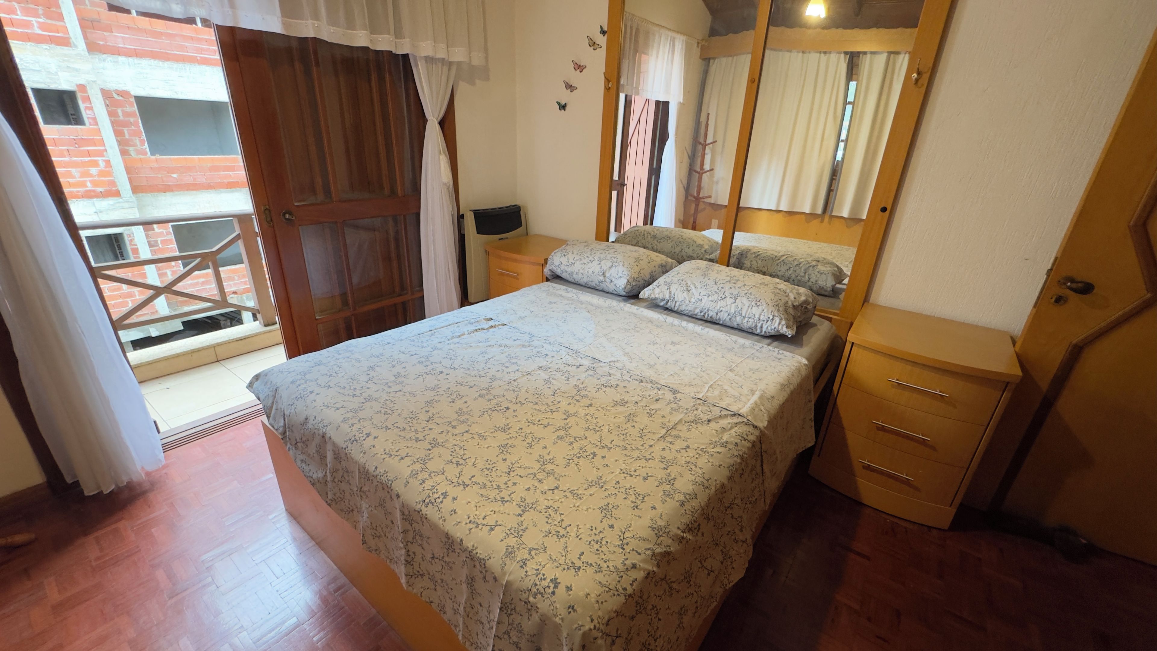 A bedroom with a bed, a nightstand, a wooden wardrobe, and a balcony door.