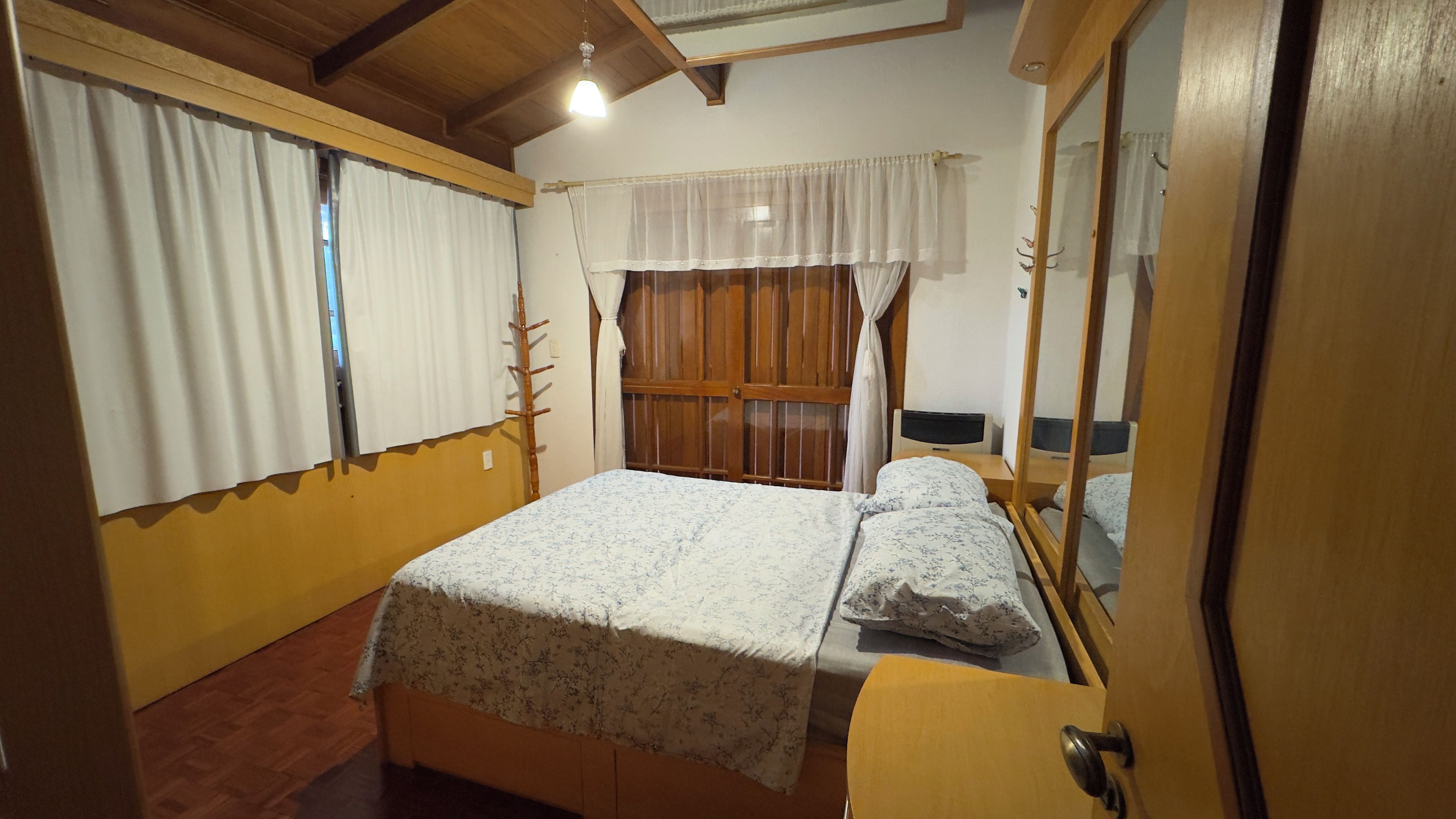 A bedroom with a bed, a bedside table, a wardrobe, and a window with curtains.