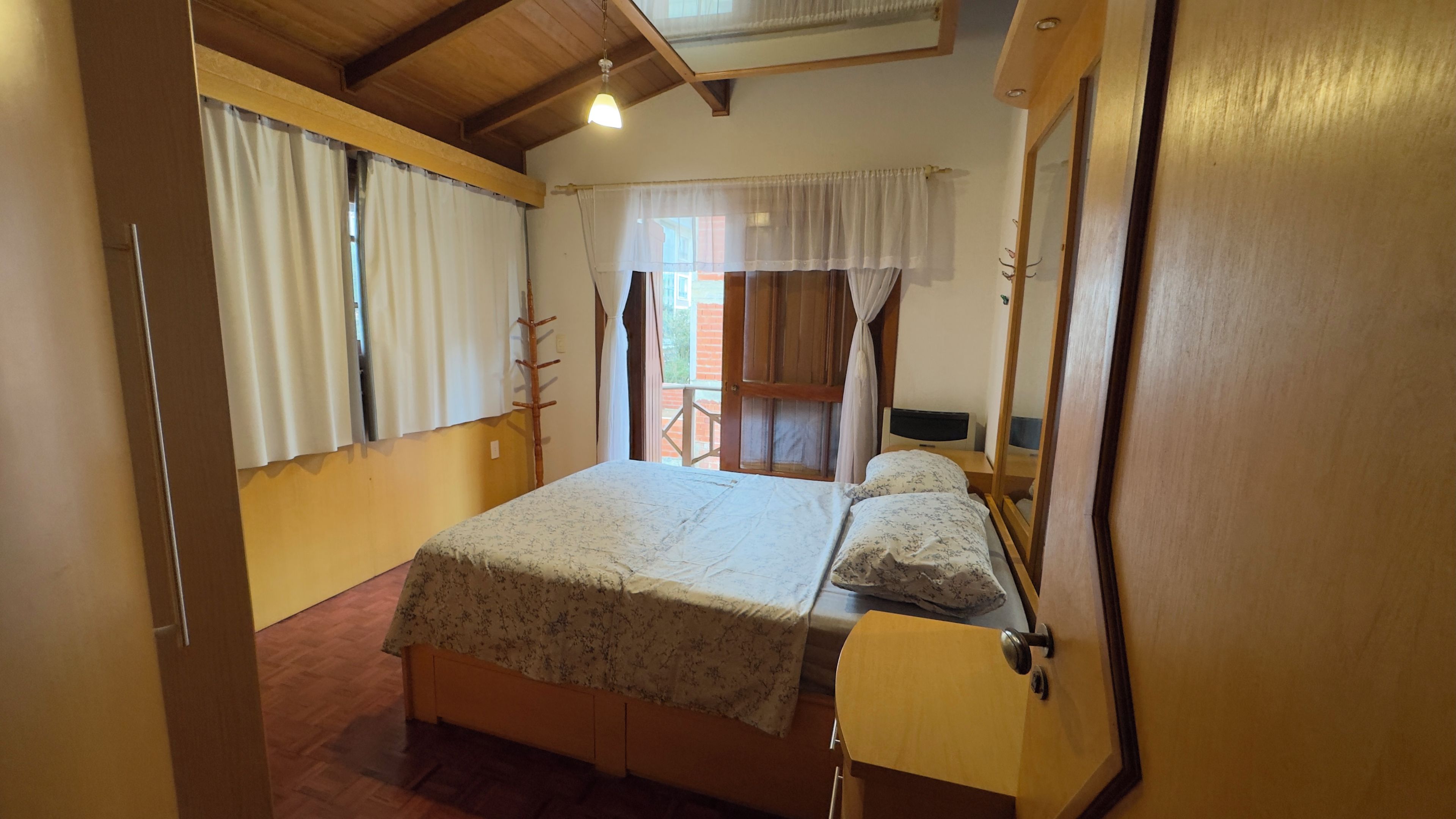 Quarto com cama, mesa de cabeceira, espelho e janela com cortinas.