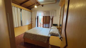 Quarto com cama, mesa de cabeceira, espelho e janela com cortinas.