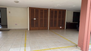 Um corredor com chão ladrilhado, portas de madeira com etiquetas e luminária fixada na parede.