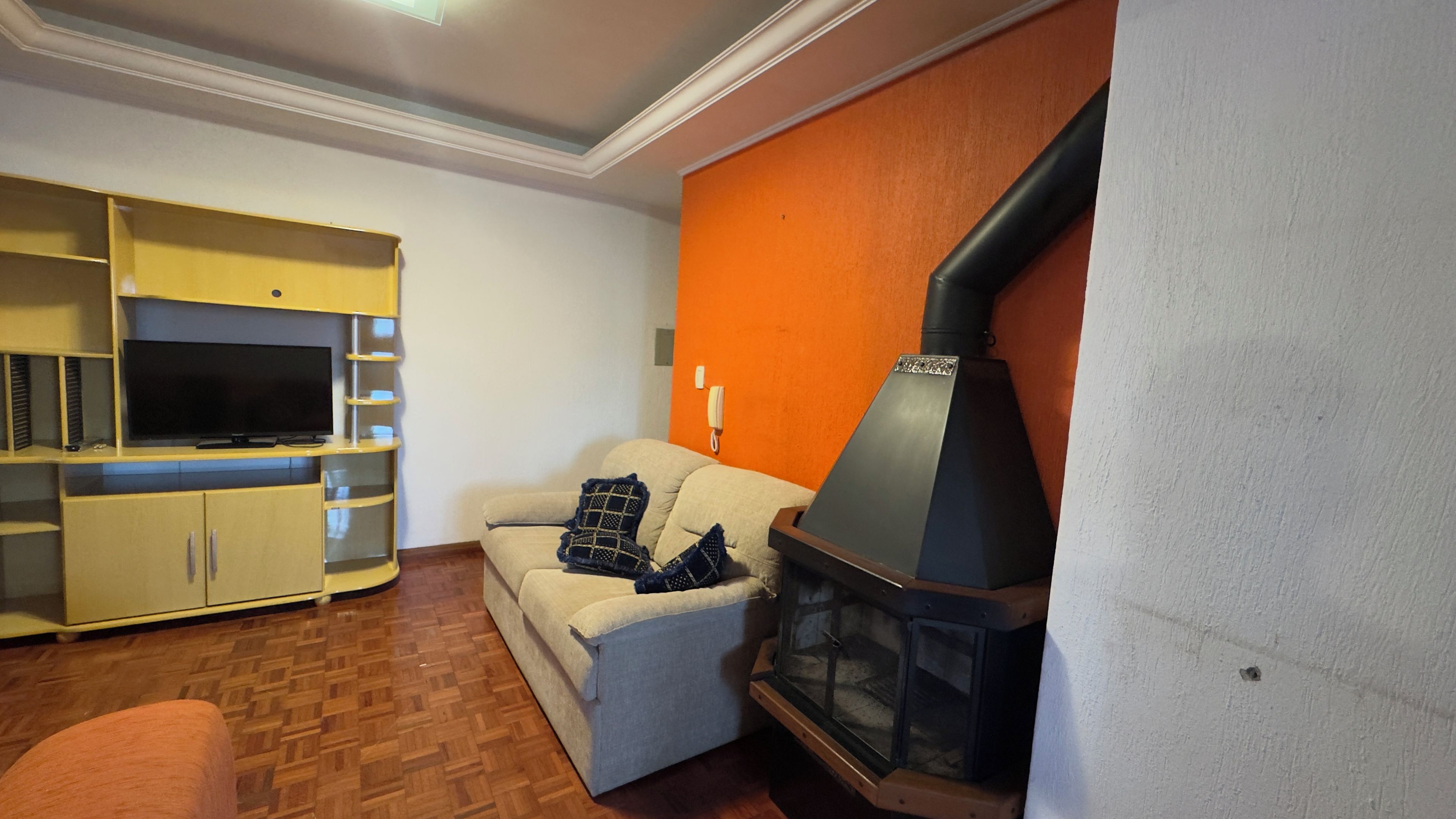 Uma sala de estar com sofá, painel para TV e lareira a lenha.