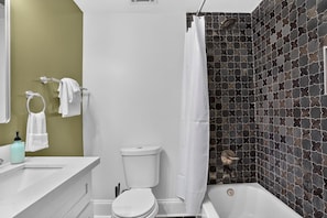 Une salle de bain avec des toilettes blanches, une baignoire et un rideau de douche.