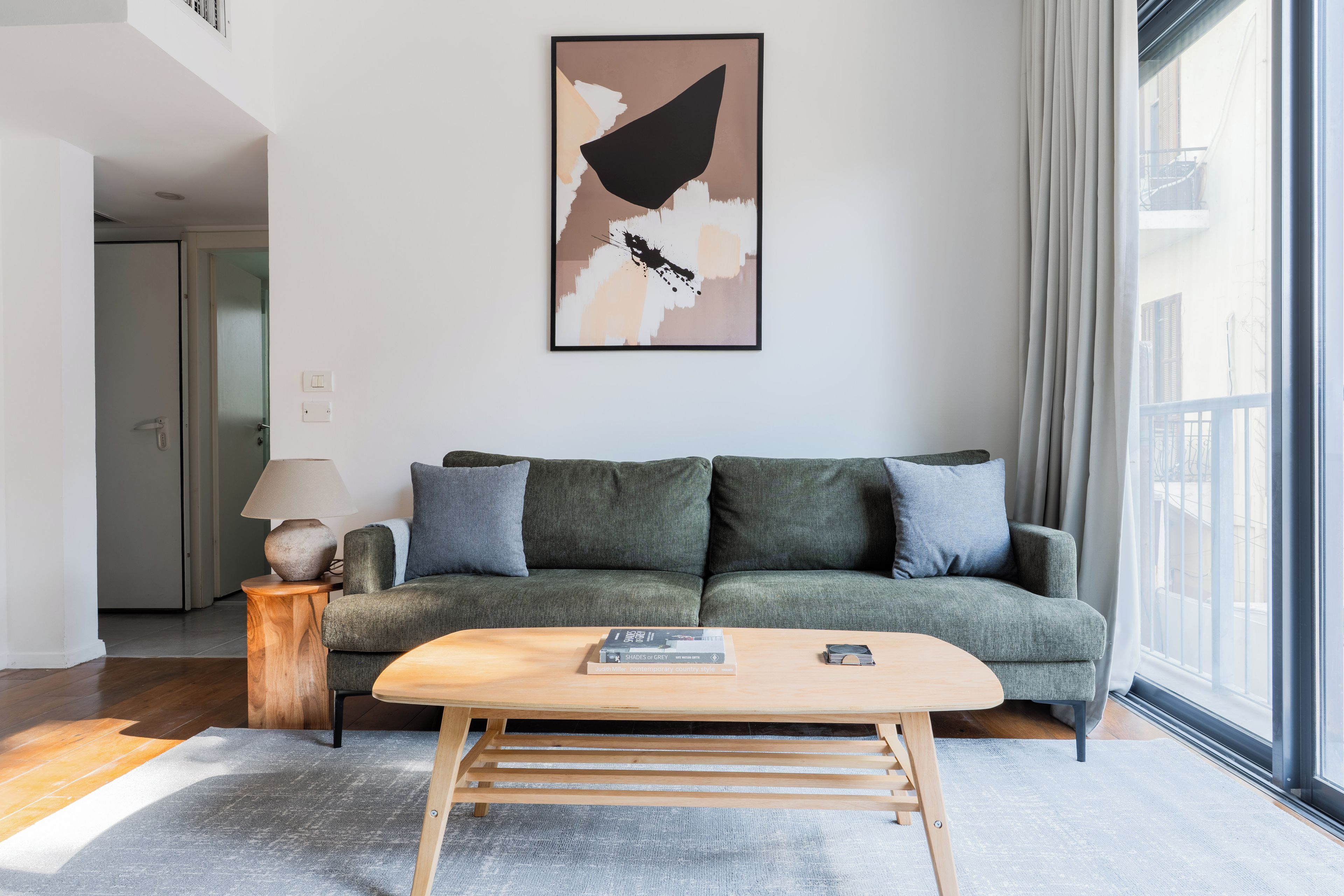 A modern living room with a green sofa, a wooden coffee table, and a large abstract painting on the wall.