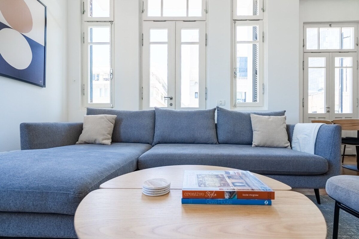 A modern living room with a grey sectional sofa, a round wooden coffee table, and a book titled 'Creative Style' by Lizzie McGraw.