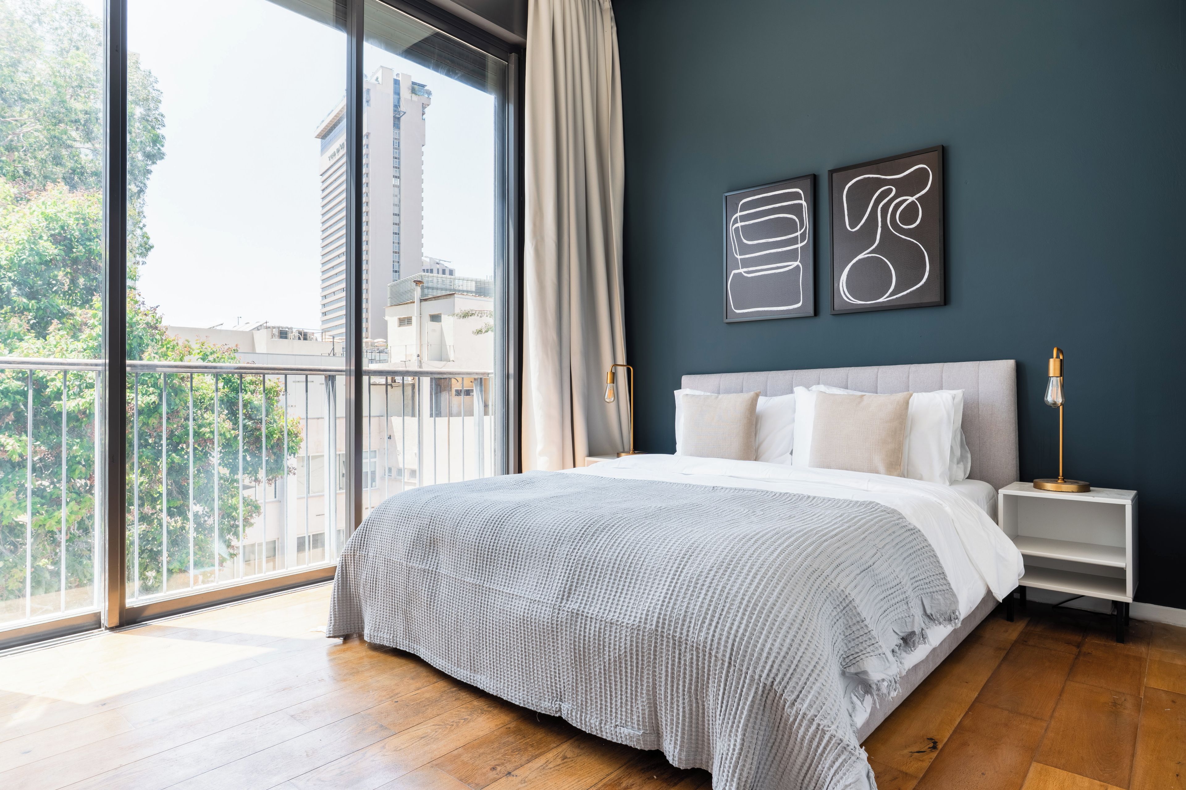 Een slaapkamer met een groot bed, een nachtkastje en uitzicht op een stadsgezicht vanaf een balkon.