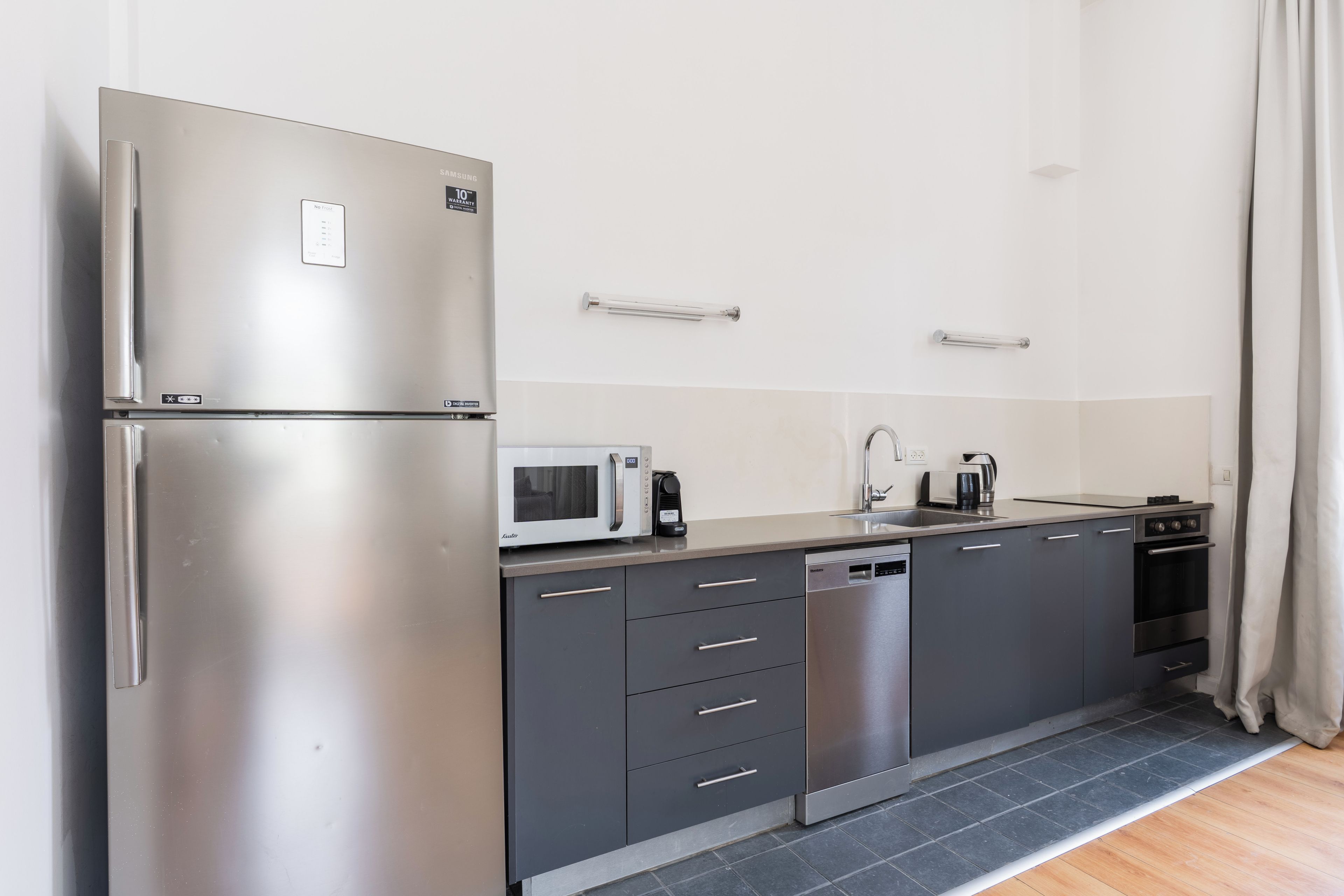 A modern kitchen with a stainless steel refrigerator, microwave, dishwasher, and a built-in oven.
