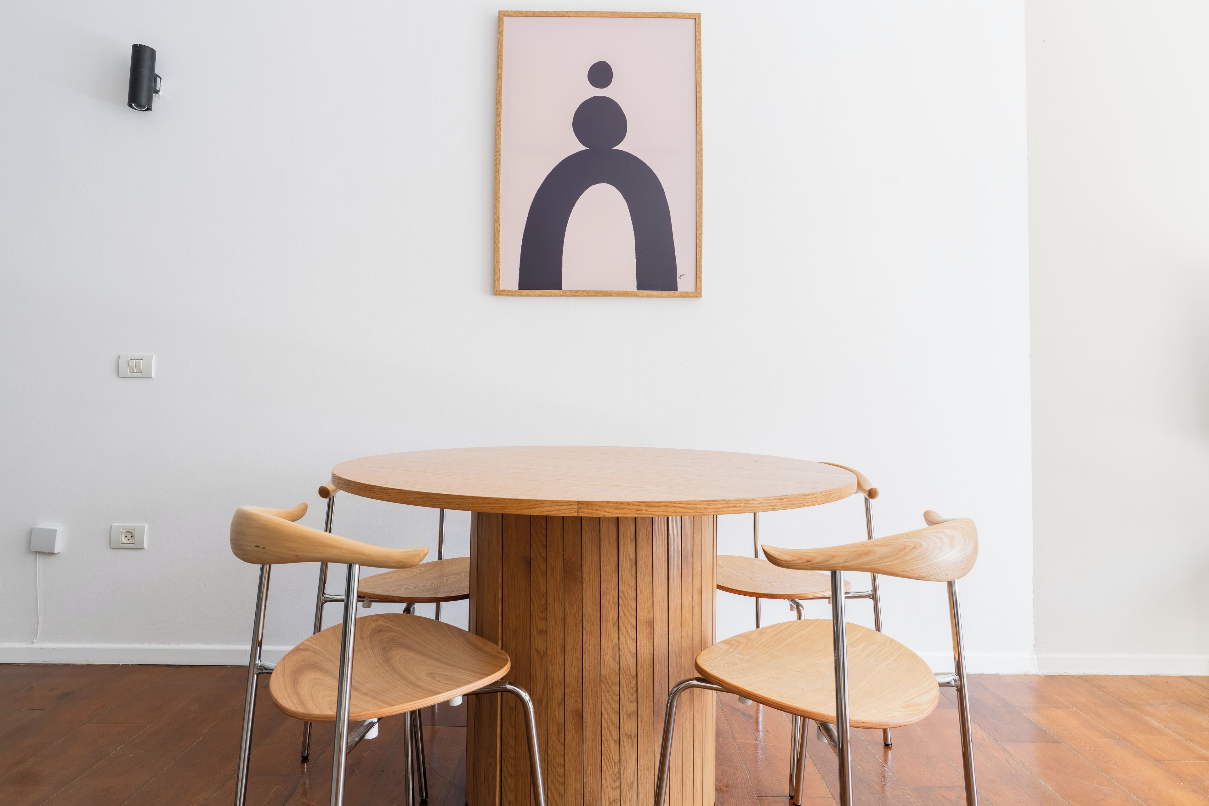 Een ronde houten tafel met vier stoelen, een stopcontact en een lijst met abstracte kunst erboven.