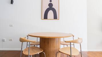 Een ronde houten tafel met vier stoelen, een stopcontact en een lijst met abstracte kunst erboven.