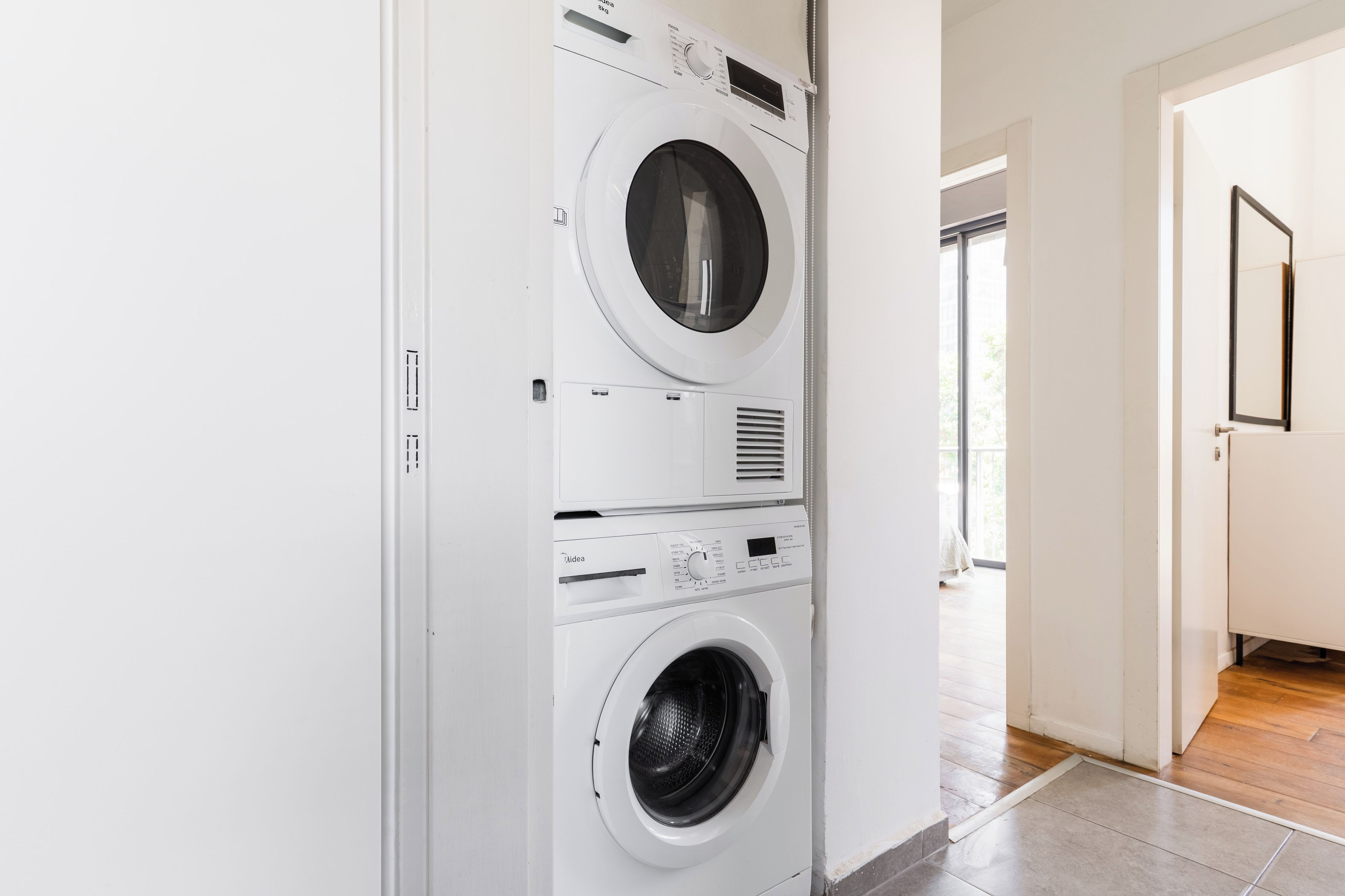 A laundry room with two stacked washing machines and a dryer, a tiled floor, and a doorway leading to another room.