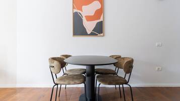 Un área de comedor con una mesa redonda y seis sillas, un cuadro abstracto enmarcado en la pared, y una lámpara de pared.