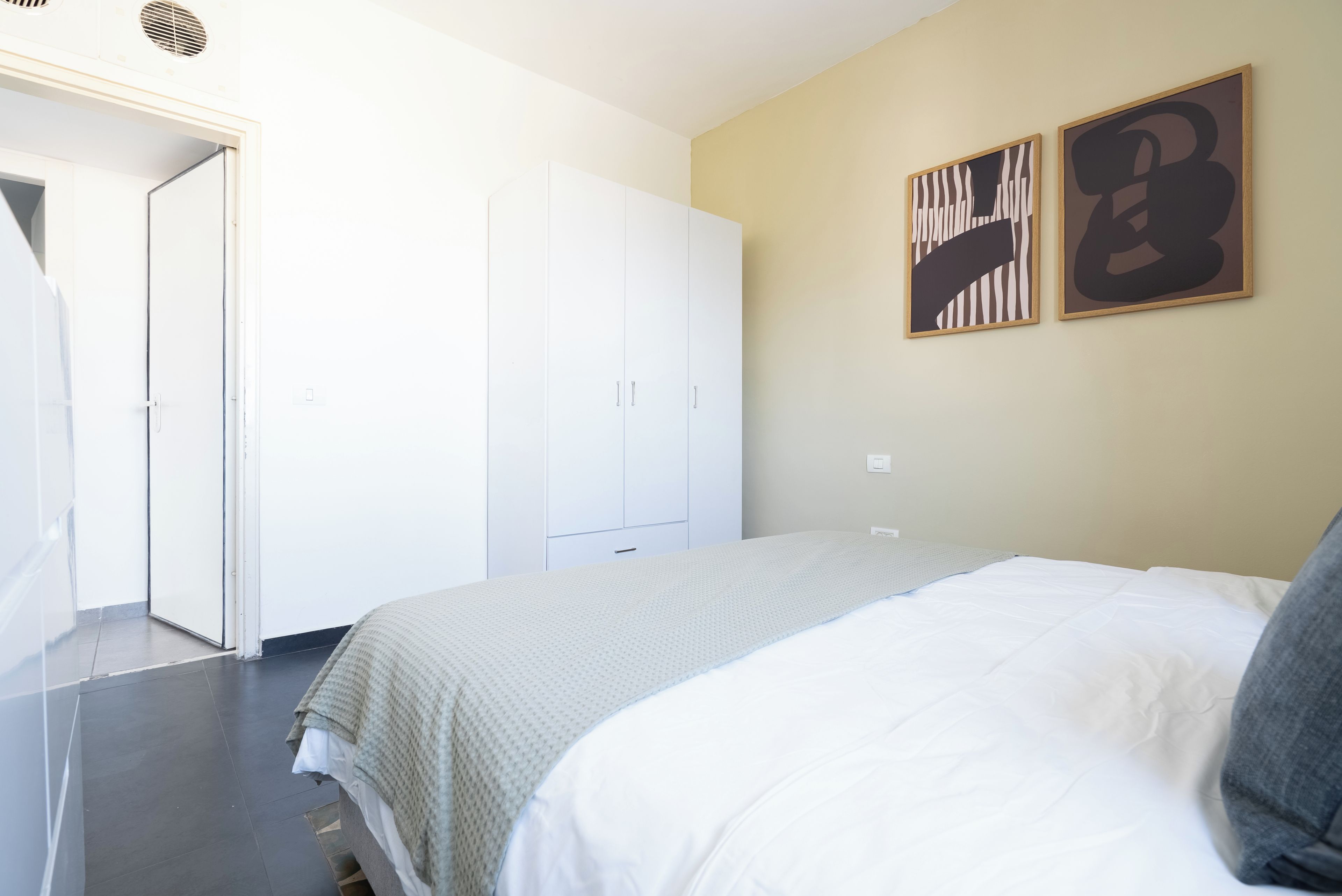 A bedroom with a bed, a wardrobe, and two wall-mounted artworks.