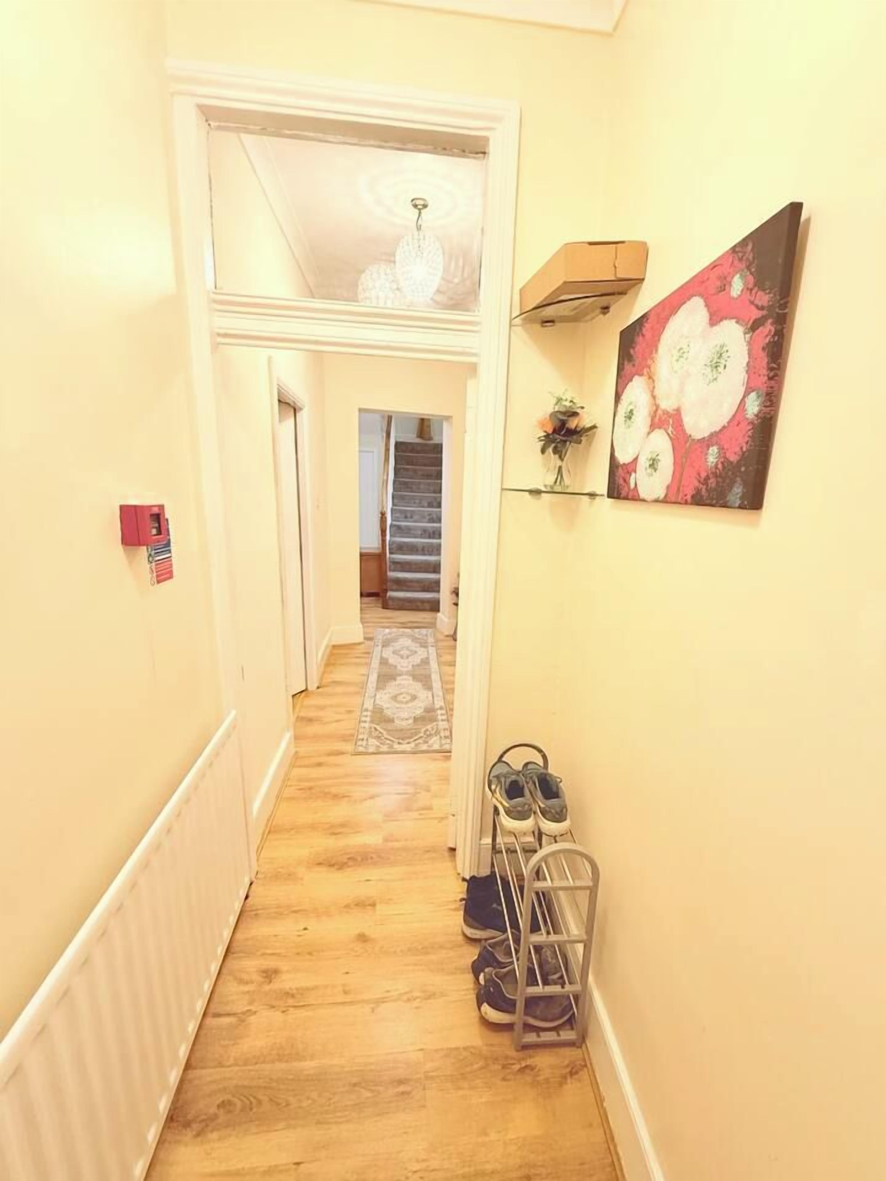 Un couloir avec un plancher en bois, un meuble à chaussures et un tableau accroché au mur.