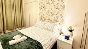 Ein Hotelzimmer mit einem Bett, einem Nachttisch mit Lampe und Blumenvase sowie einem Fenster mit Vorhängen.