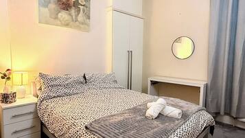 A neatly made bed with a leopard print bedspread, a bedside lamp, and a small table with a mirror.