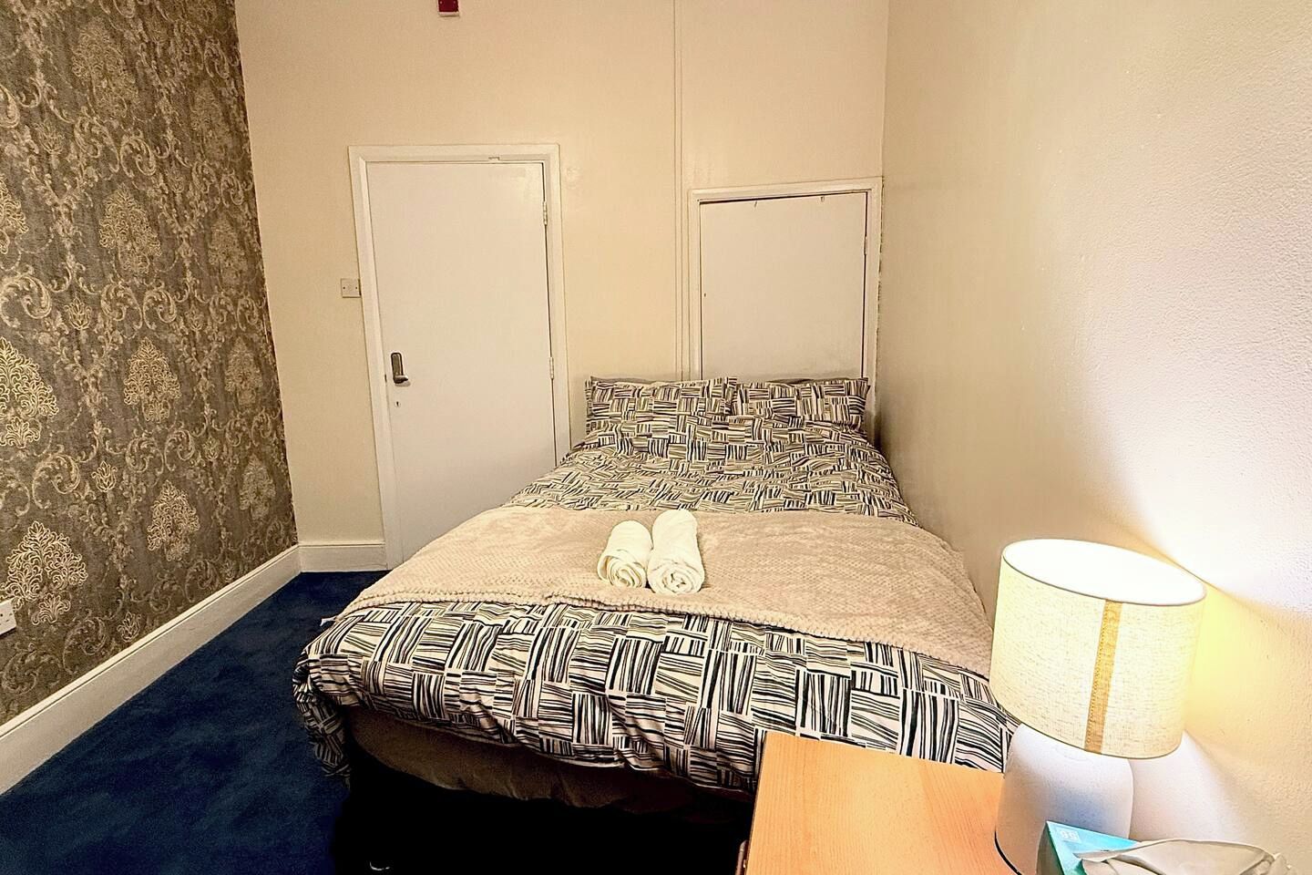 Une chambre d’hôtel avec un lit, une table de chevet, une lampe et une porte.