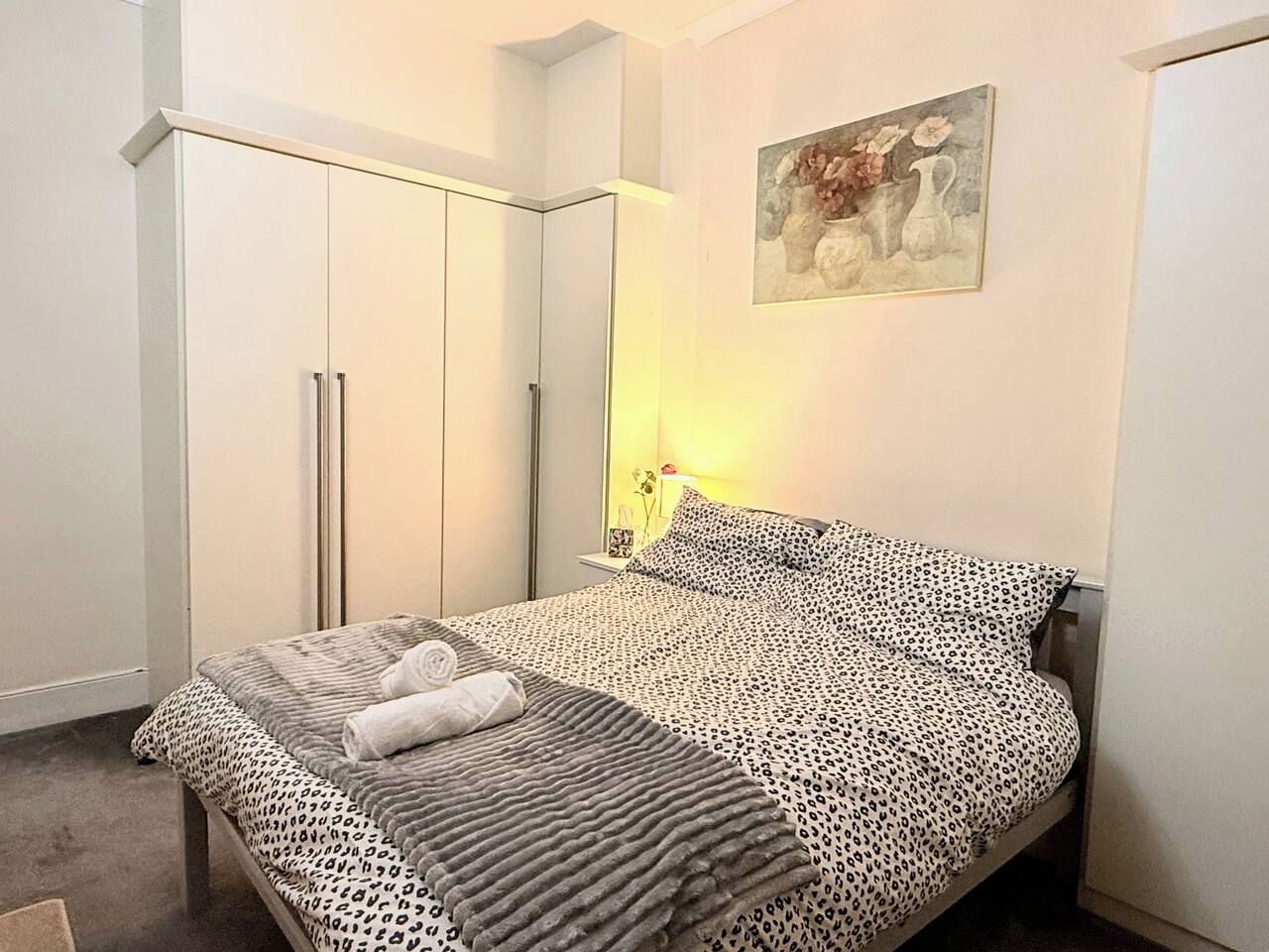 Une chambre à coucher avec un lit, une armoire, une table de chevet et un tableau accroché au mur.