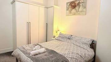 Een slaapkamer met een bed, een kledingkast, een nachtkastje en een schilderij aan de muur.